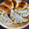 Gyoza japonais disposés sur une assiette en bois, 4 d'entre eux montrent leur côté roussi