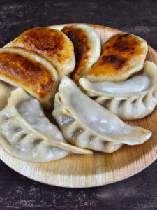 Gyoza japonais disposés sur une assiette en bois, 4 d'entre eux montrent leur côté roussi