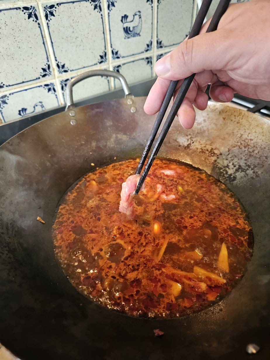 morceau de viande tenu par des baguettes au-dessus d'un bouillon du Sichuan rouge