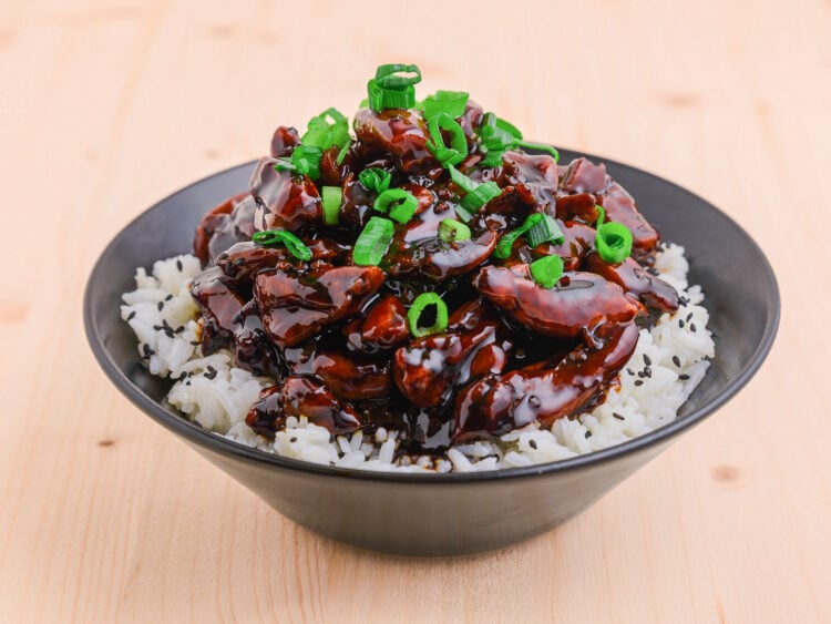 Poulet teriyaki dans un bol sur du riz sur fond de bois avec jeunes