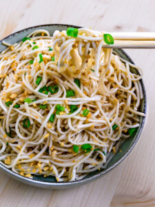 Nouilles à l'ail frit dans un bol soulevées par des baguettes sur fond de bois