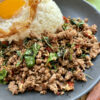 boeuf sauté au basilic thaï sur une assiette sombre accompagné de riz et d'un oeuf frit