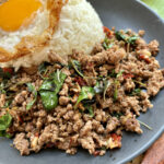 boeuf sauté au basilic thaï sur une assiette sombre accompagné de riz et d'un oeuf frit