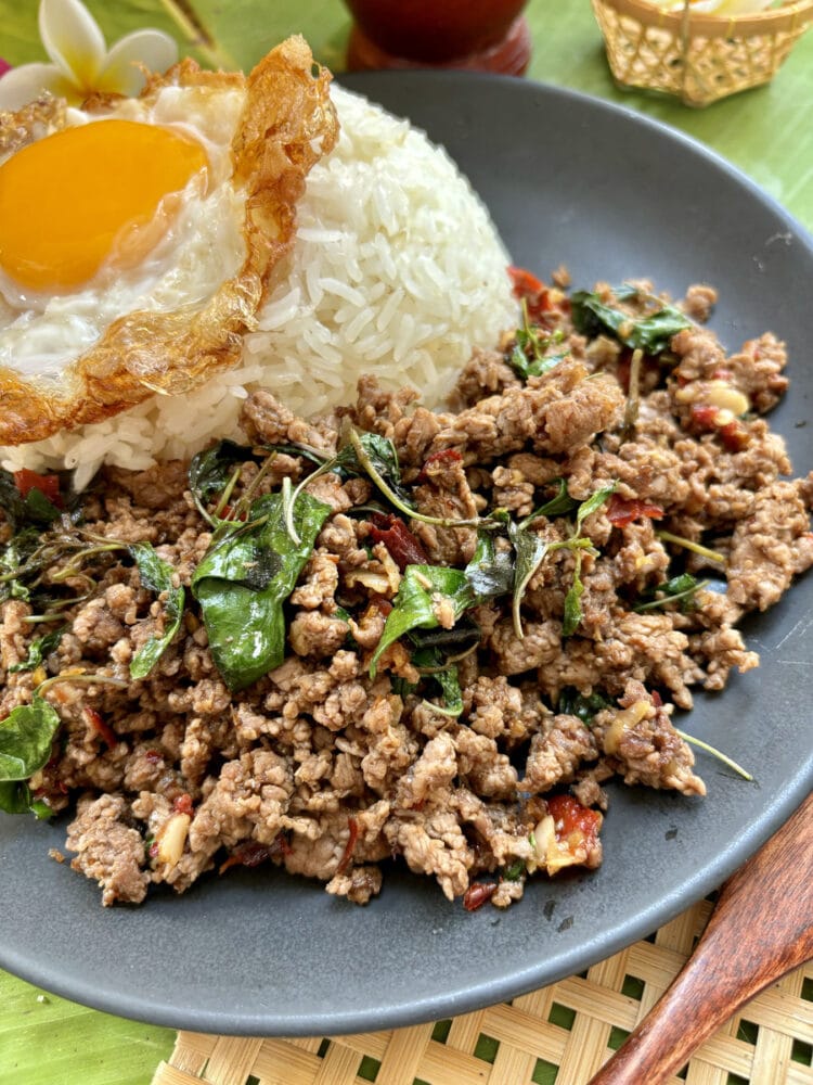 boeuf sauté au basilic thaï sur une assiette sombre accompagné de riz et d'un oeuf frit