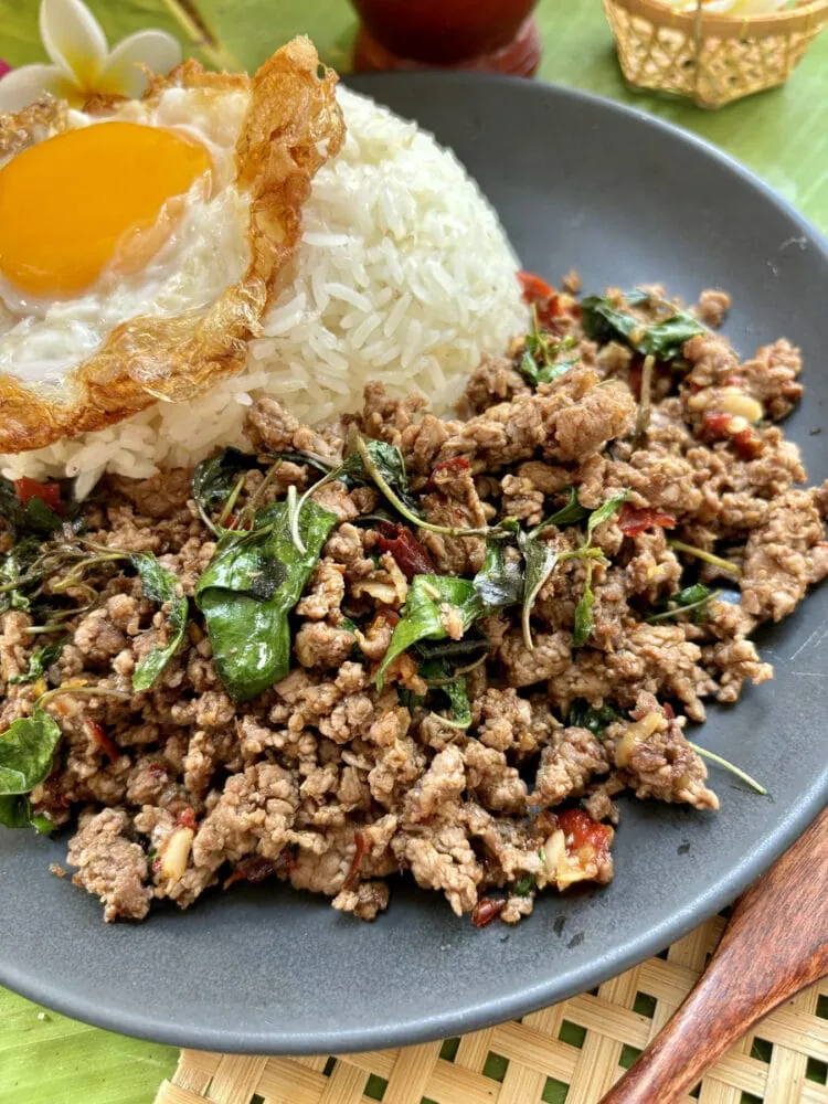 boeuf sauté au basilic thaï sur une assiette sombre accompagné de riz et d'un oeuf frit