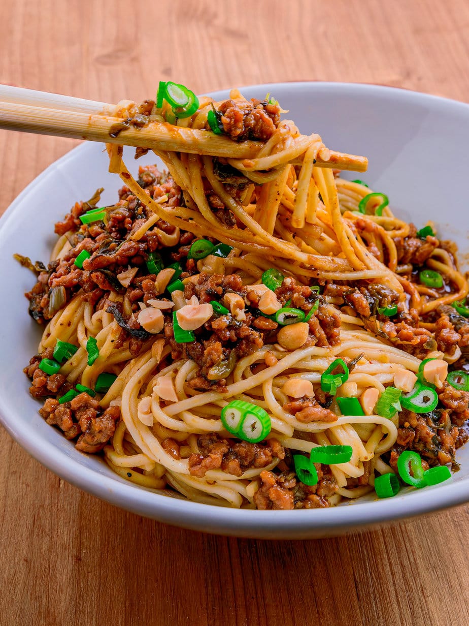 Dan dan mian noodles on a wooden background lifted by chopsticks