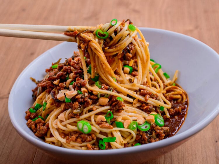 Nouilles dan dan mian sur fond de bois soulevées par des baguettes