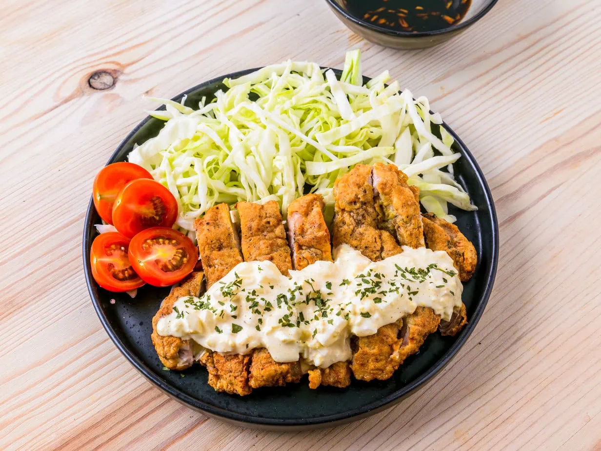 Poulet nanban sur une assiette noire sur fond de bois