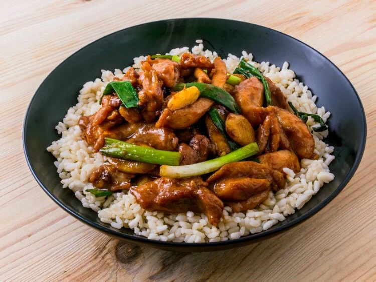 poulet sacha dans un bol noir sur du riz avec fond de bois