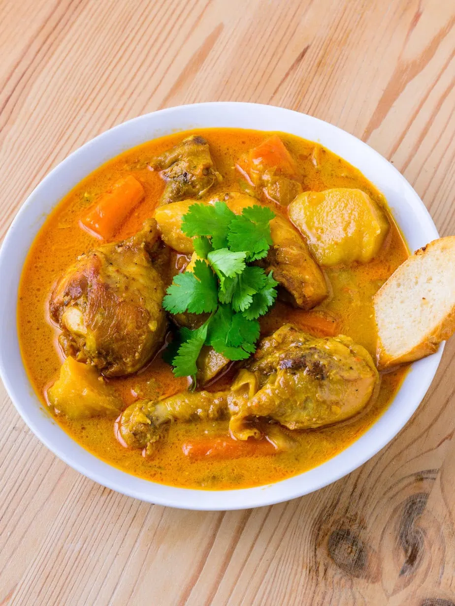 Vietnamese chicken curry in a white bowl on a wooden background with a baguette