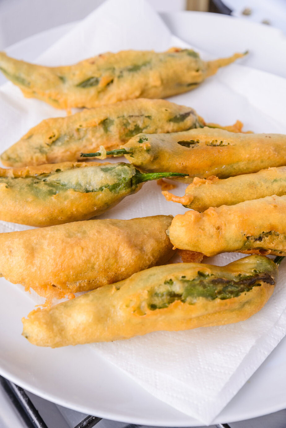 Piments verts frits enrobés de pâte, servis sur une assiette avec du papier absorbant.