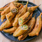 Piments verts frits enrobés de pâte, servis sur une assiette avec du papier absorbant.