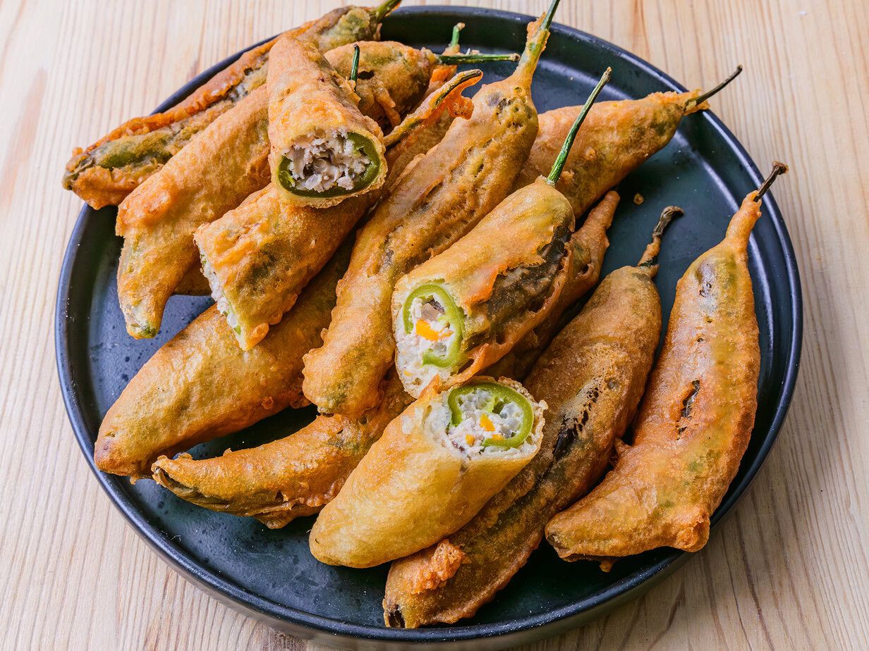 Piments verts frits enrobés de pâte, servis sur une assiette avec du papier absorbant.