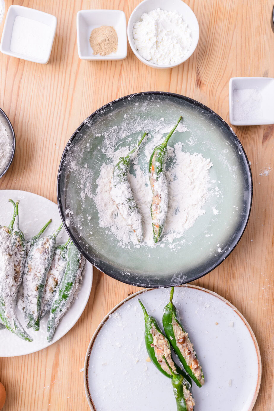 Piments verts farcis enrobés de farine, prêts à être cuisinés, sur une table en bois avec des ingrédients.