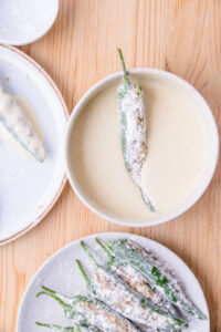 Piments farcis enrobés de farine, prêts à être trempés dans une pâte à frire sur une table en bois.