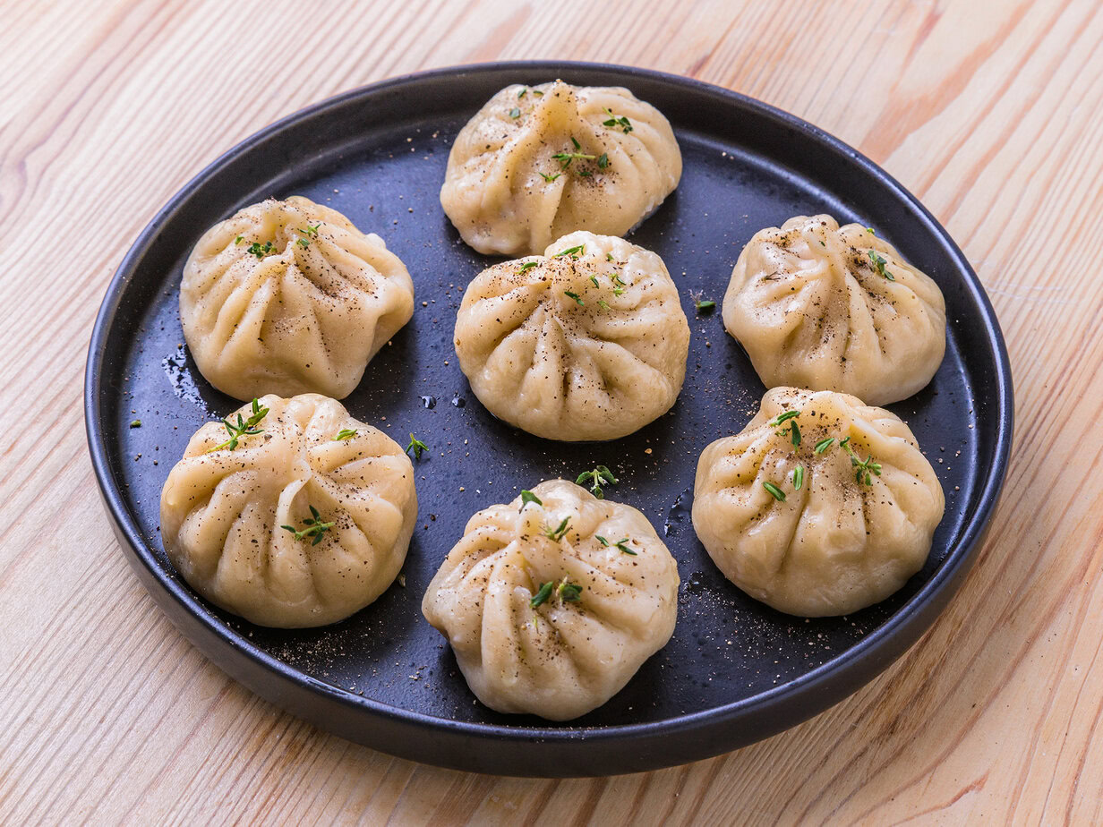 Assortiment de raviolis garnis, servis sur une assiette noire, saupoudrés d’herbes et de poivre.