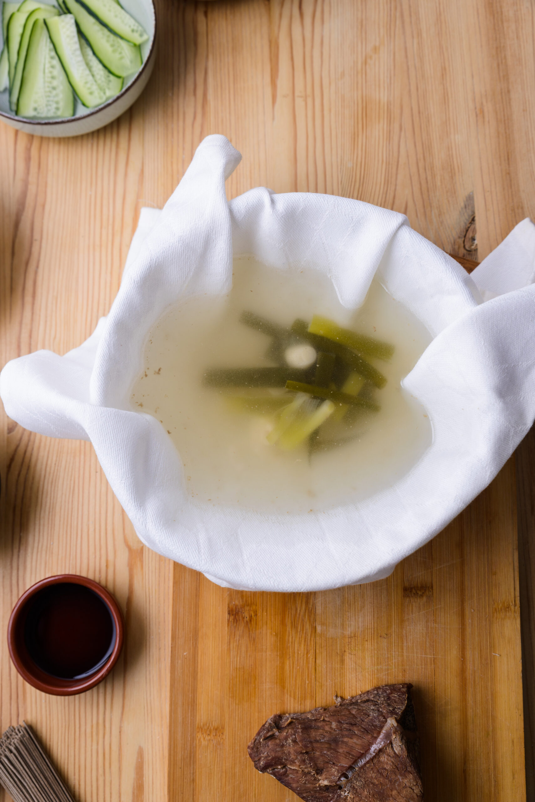 Bouillon filtré dans un linge blanc, avec des légumes, sur une table en bois.