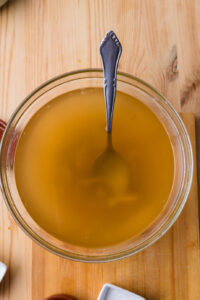 Bol de bouillon clair avec une cuillère, posé sur une table en bois.