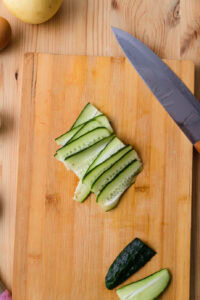 Tranches de concombre sur une planche à découper en bois avec un couteau à côté.