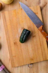 Morceau de concombre salé sur une planche à découper en bois avec un couteau à côté.