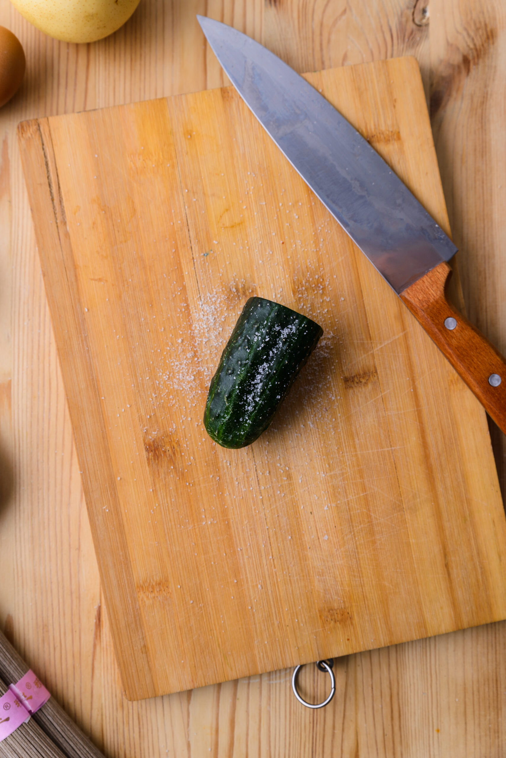 Morceau de concombre salé sur une planche à découper en bois avec un couteau à côté.