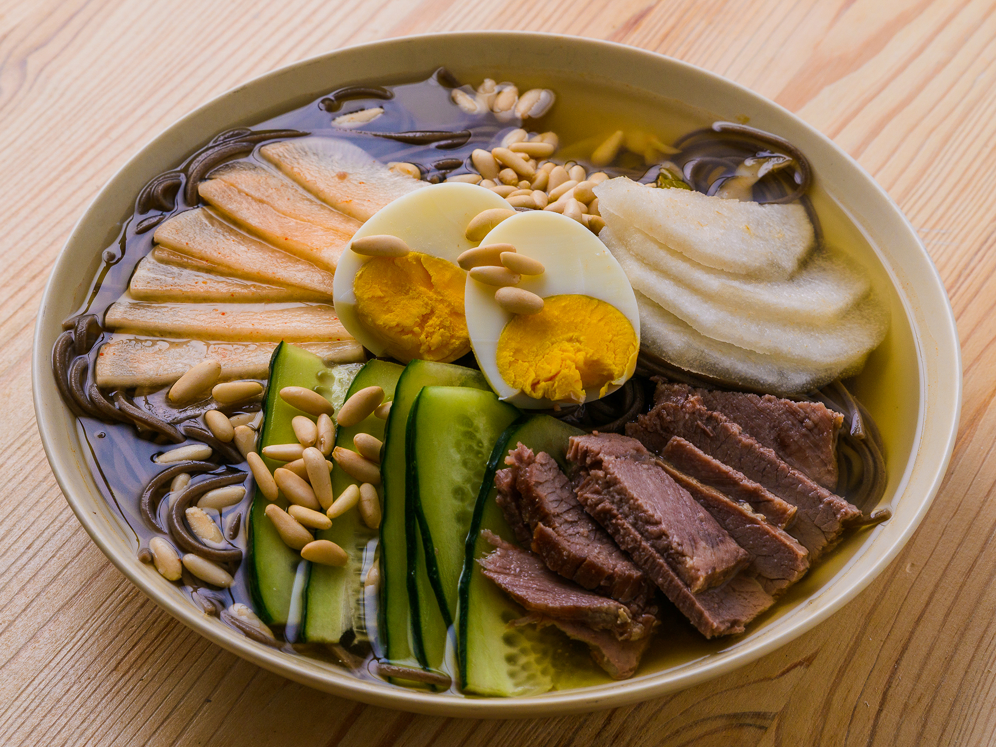Bol de nouilles froides coréennes avec bœuf, œuf, concombre, poire, pignons et bouillon clair.