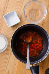 Casserole avec sauce rouge et cuillère, bols de sel et de lait sur une table en bois.