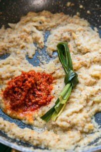 Pâte d’épices sautée avec purée de piment rouge et feuille de pandan nouée dans une poêle.