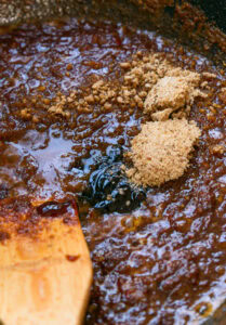 Cassonade et sauce mélangées dans une poêle avec une spatule en bois.