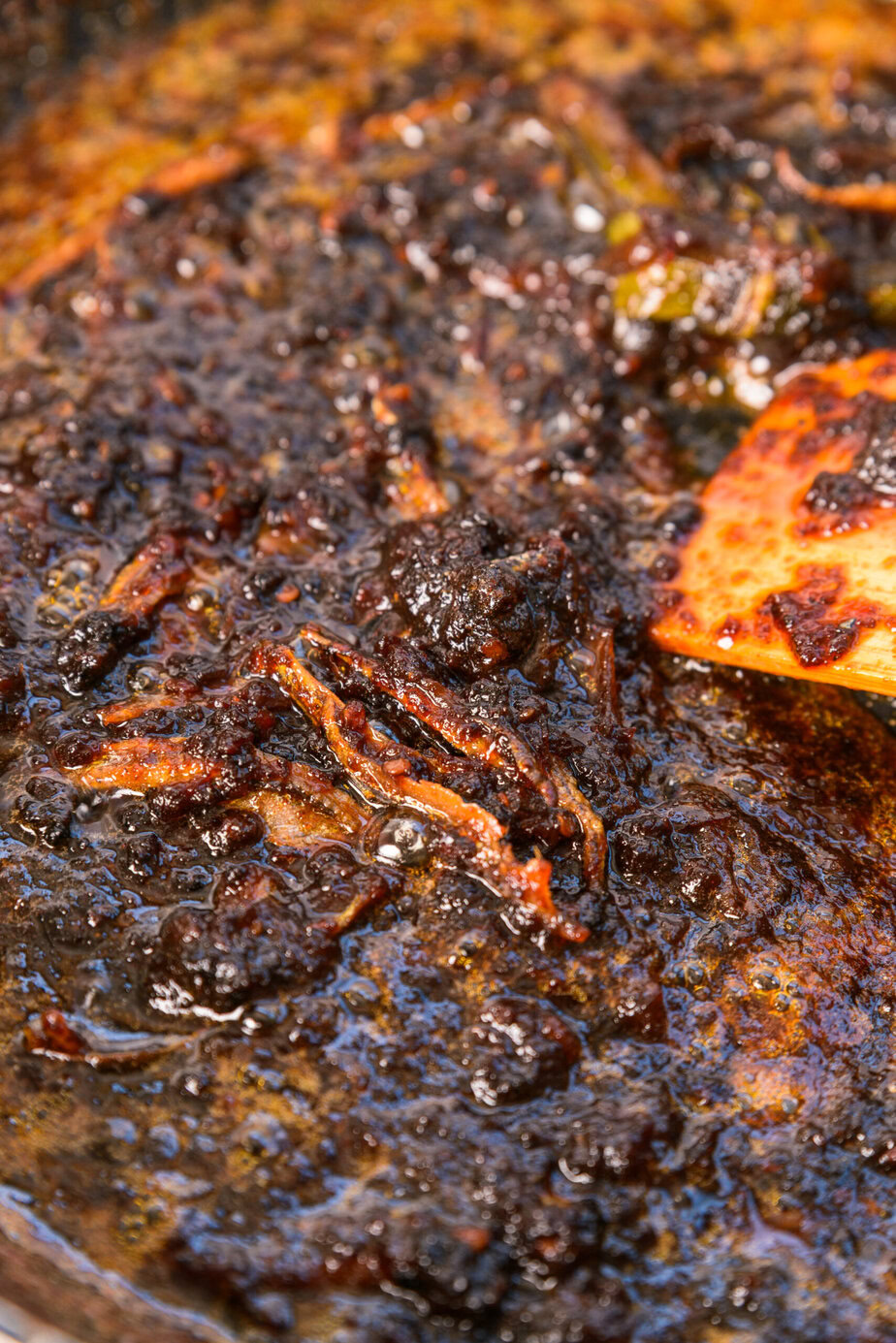 木べらでかき混ぜながら煮込む濃くてとろみのあるソースのクローズアップ。