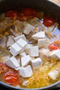 Cubes de tofu ajoutés dans une soupe avec tomates et morceaux de viande.