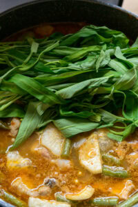 Feuilles de légumes vertes fraîches sur une soupe mijotée avec légumes et bouillon orangé.