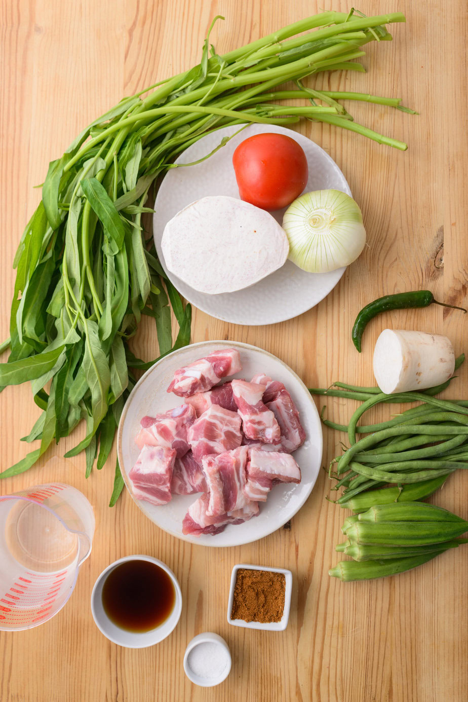 Ingrédients variés sur une table : légumes, viande, épices, sauce, eau et condiments.