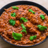 Curry de poulet rouge garni de coriandre fraîche dans une assiette noire sur une table en bois.
