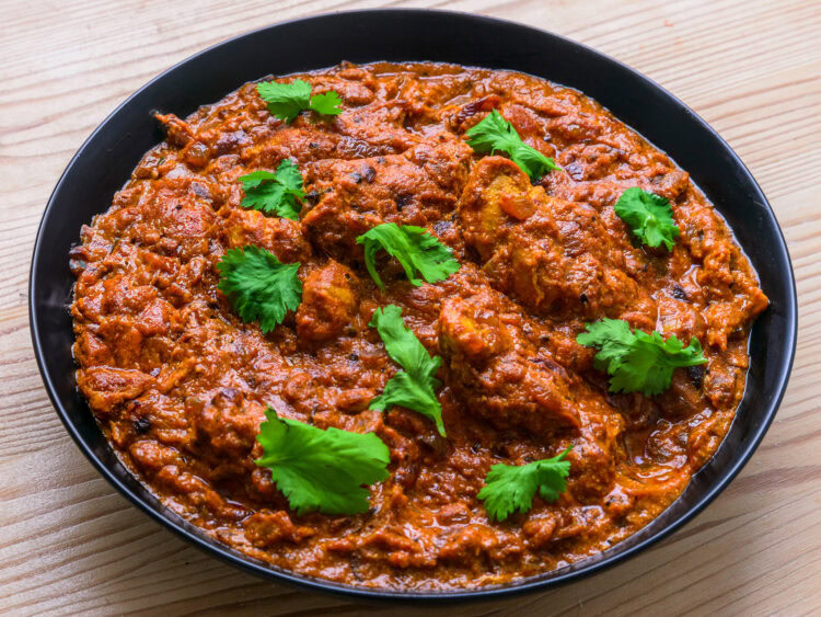 Curry de poulet rouge garni de coriandre fraîche dans une assiette noire sur une table en bois.