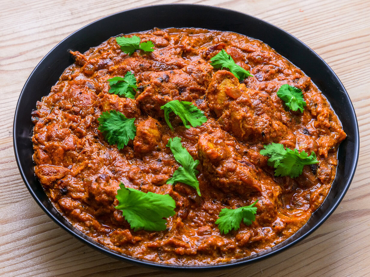 Curry de poulet rouge garni de coriandre fraîche dans une assiette noire sur une table en bois.
