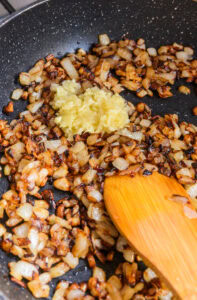 Oignons dorés et ail râpé dans une poêle, remués avec une spatule en bois.