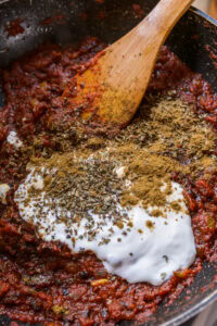 Sauce tomate mijotée avec crème, herbes et épices, mélangée avec une cuillère en bois dans une poêle.