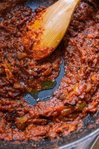 Sauce tomate épaisse en cuisson dans une poêle, remuée avec une spatule en bois.