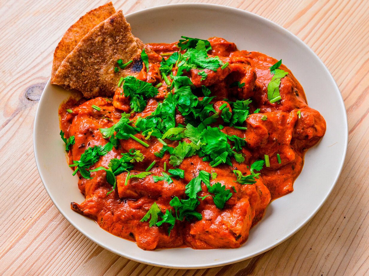 Poulet tikka masala garni de coriandre fraîche, servi avec des morceaux de pain naan dans une assiette blanche.