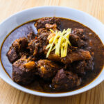 Ragoût de viande en sauce brune, garni de lamelles de gingembre, servi dans une assiette blanche.