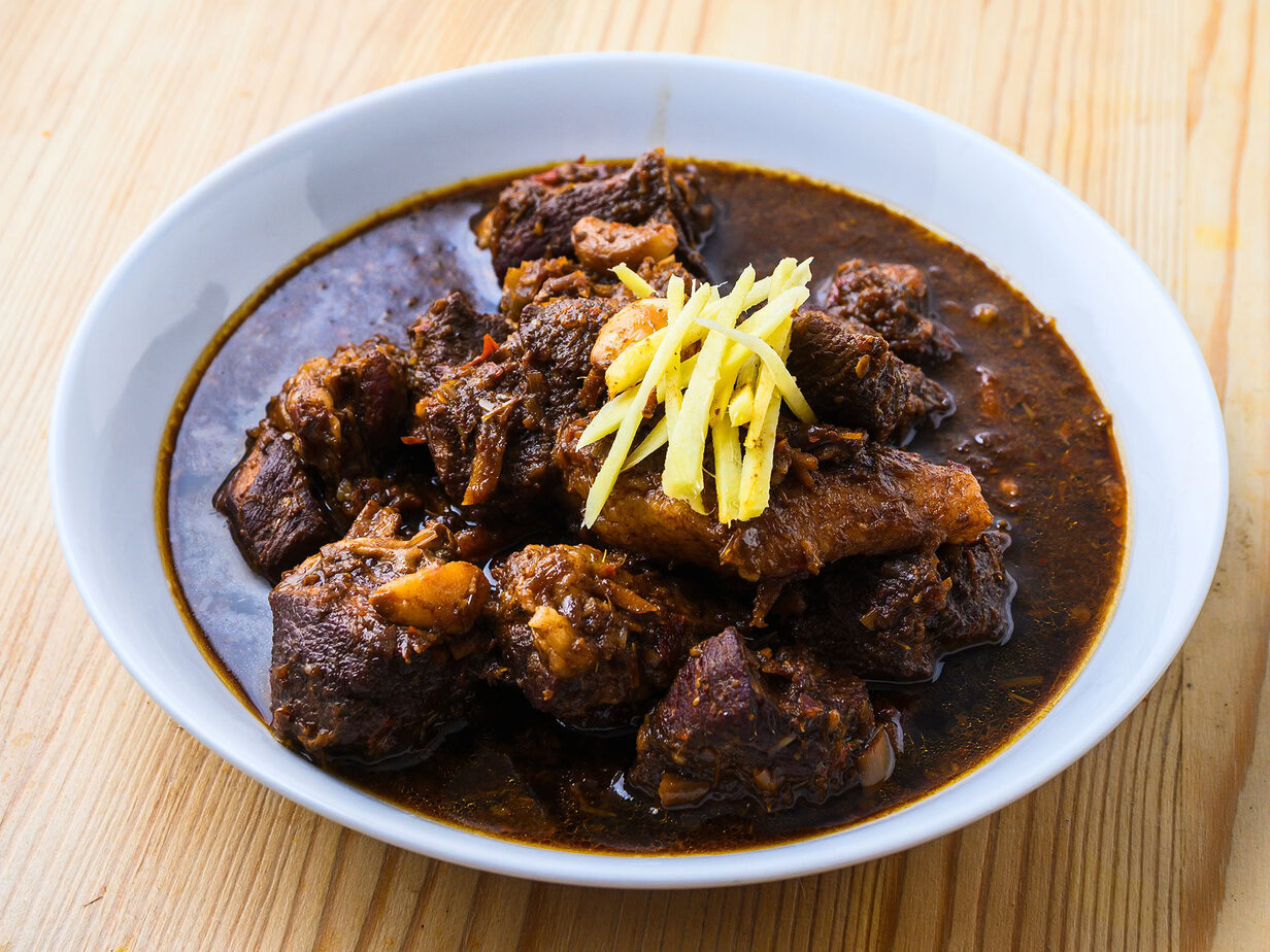 Ragoût de viande en sauce brune, garni de lamelles de gingembre, servi dans une assiette blanche.