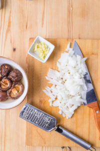 Oignons hachés, couteau, gingembre râpé, champignons dans un bol et râpe sur une planche en bois.