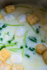 Soupe crémeuse avec boulettes blanches, cubes de tofu frit et herbes vertes.
