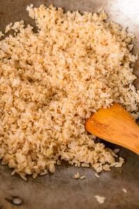 Khao Kluk Kapi - Ajouter le riz enrobé de pâte de crevettes et faire sauter à feu moyen jusqu’à ce qu’il soit bien chaud et aromatique. (Sauter d’abord la pâte de crevettes puis ajouter le riz, si souhaité.)