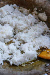 Riz blanc cuit dans une poêle avec un peu d’huile et une spatule en bois.