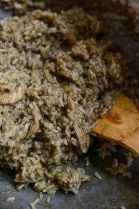 Riz crémeux mélangé avec des morceaux de viande, remué avec une cuillère en bois.