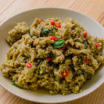 Riz sauté au curry vert avec morceaux de viande, basilic et piment rouge dans une assiette blanche.