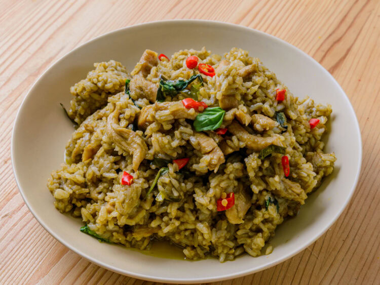 Riz sauté au curry vert avec morceaux de viande, basilic et piment rouge dans une assiette blanche.
