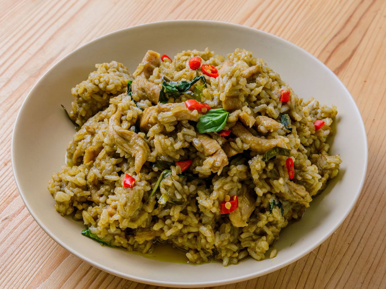 Riz sauté au curry vert avec morceaux de viande, basilic et piment rouge dans une assiette blanche.